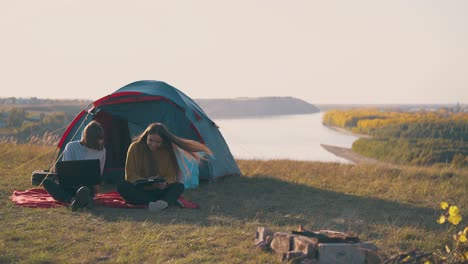 women-hikers-with-tablet-and-laptop-on-red-plaid-near-tent