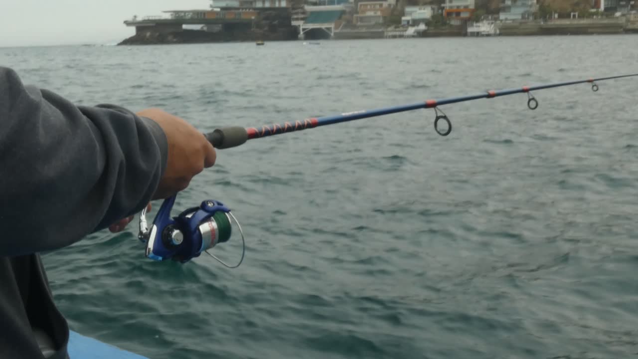A fisherman angling with his fishing rod. He stands on the edge of a boat waiting to catch a fish. Recorded in Lima, Peru in "Punta Hermosa" beach