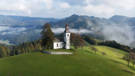 scenic clouds rolling on early morning with church of sveti tomaz near skofja loka in slovenia