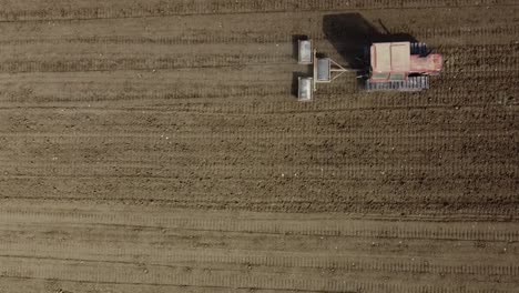 Tractor-De-Orugas-Rojas-Con-Máquina-De-Triple-Rollo-Arando-La-Tierra-En-Una-Granja-Agrícola,-Vista-Aérea-Minimalista-De-Arriba-Hacia-Abajo