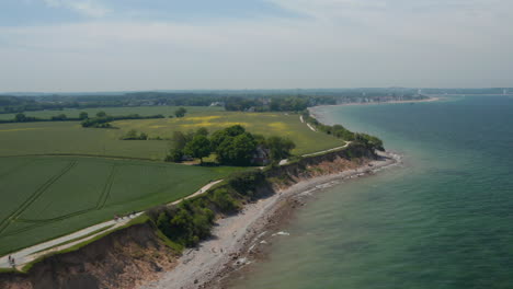 Circle-pan-aerial-drone-view-of-shoreline-beach-with-vast-green-field-in-Brodten,-Germany-on-peaceful-spring-day