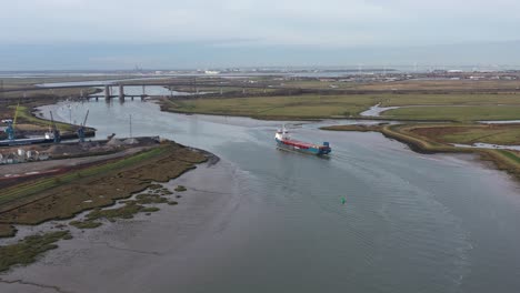 Wide-aerial-tracking-shot-of-a-ship-exporting-goods,-sailing-along-the-Swale-Estuary