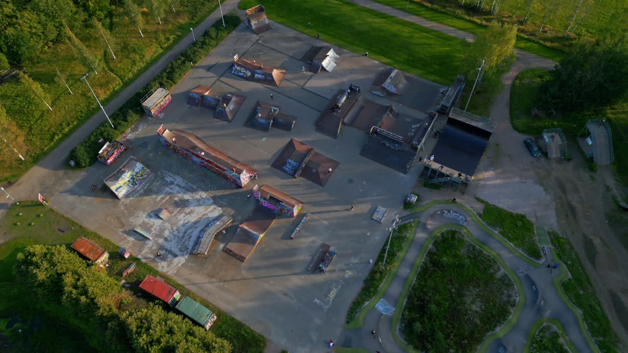 gran parque de patinaje de madera en un parque, con varias personas montando patinetas, scooters y bicicletas bmx, cámara acercándose