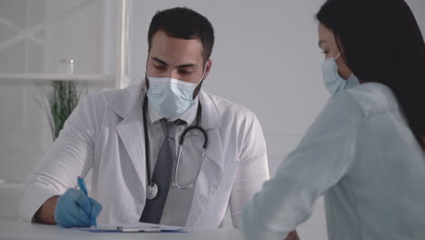 Young-male-doctor-wearing-a-medical-face-mask-treating-female-patient-at-the-office