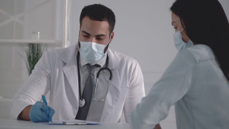 young male doctor wearing a medical face mask treating female patient at the office