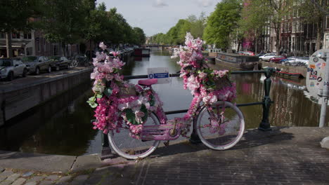 a pink bicycle decorated with flowers on the canal bridge in amsterdam, netherlands. static shot