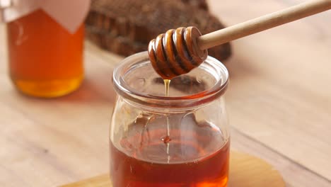 honey dripping from a wooden dipper into a glass jar