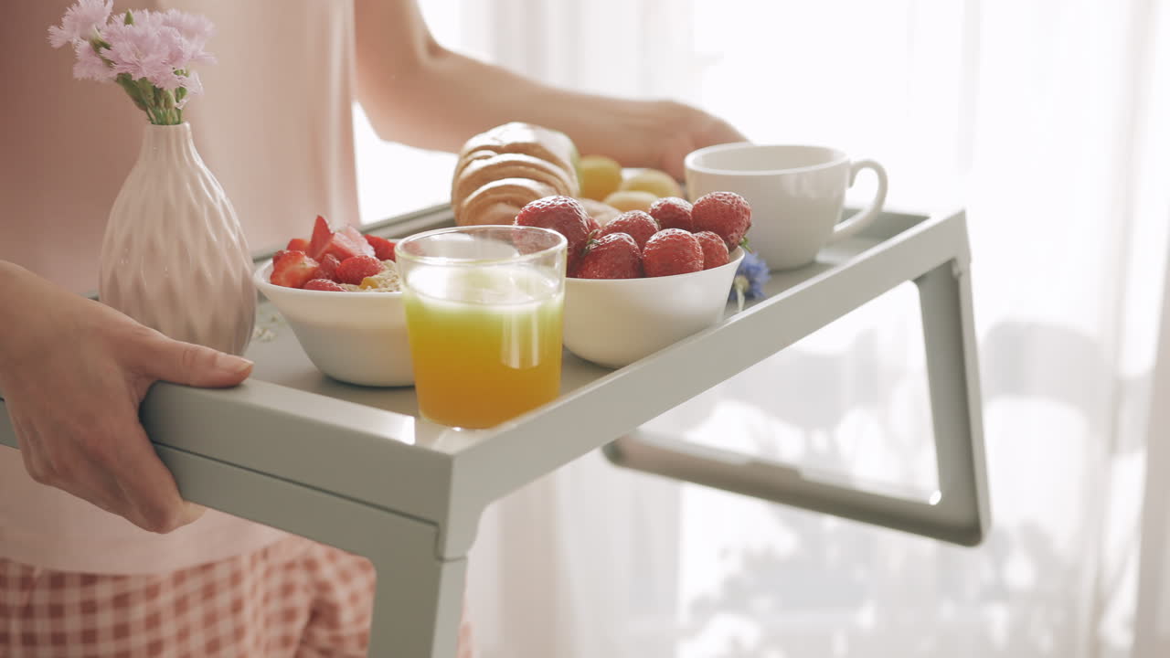 明るいベッドルームで、健康的な朝食をトレーに乗せて提供する女性