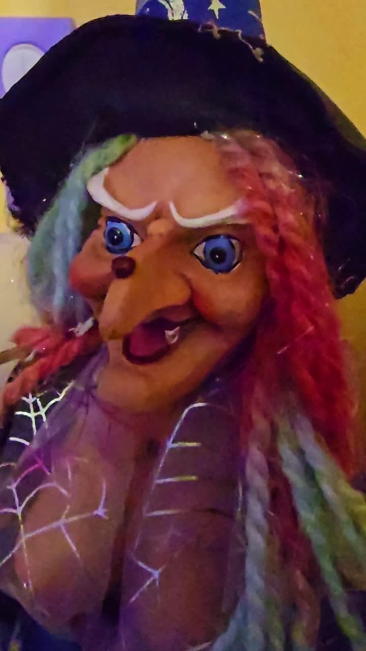 Vertical shot of a witch doll with blue eyes, green and orange hair, a spider web scarf, and a creepy smile
