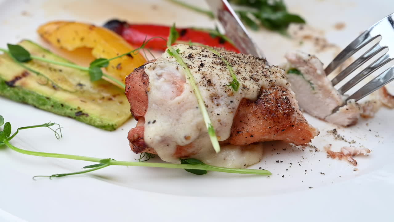 Close up of a woman eating a piece of chicken with white sauce and grilled vegetables at a restaurant