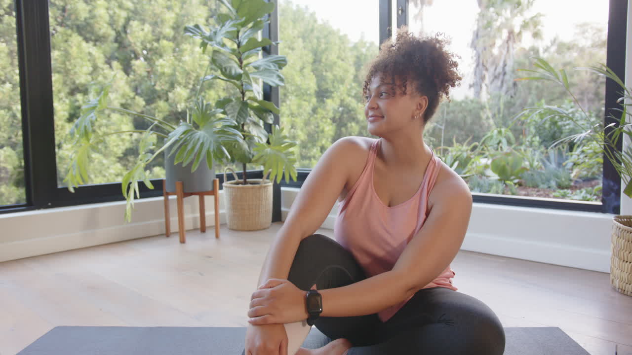 Sitting on yoga mat, plus size woman stretching and smiling in home gym