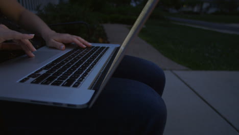 primer plano de una mujer caucásica adulta usando una computadora portátil afuera en el camino de entrada en una noche de verano