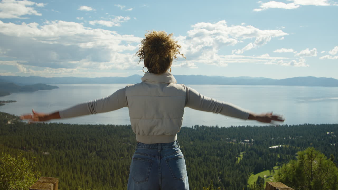 A woman stands overlooking Lake Tahoe, joyfully raising her arms to embrace the breathtaking view. Her expression of awe captures the beauty and tranquility of the stunning landscape.