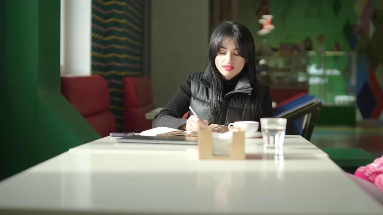 검은색 의상을 입은 전문적인 여성 관리자가 사무실을 걸어다니며 동료들과 상호 작용하며 문서와 노트북을 들고 리더십과 전문성을 보여주고 있습니다.