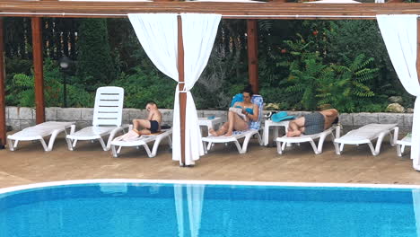 personas sentadas a la orilla de la piscina de un resort durante las vacaciones de verano