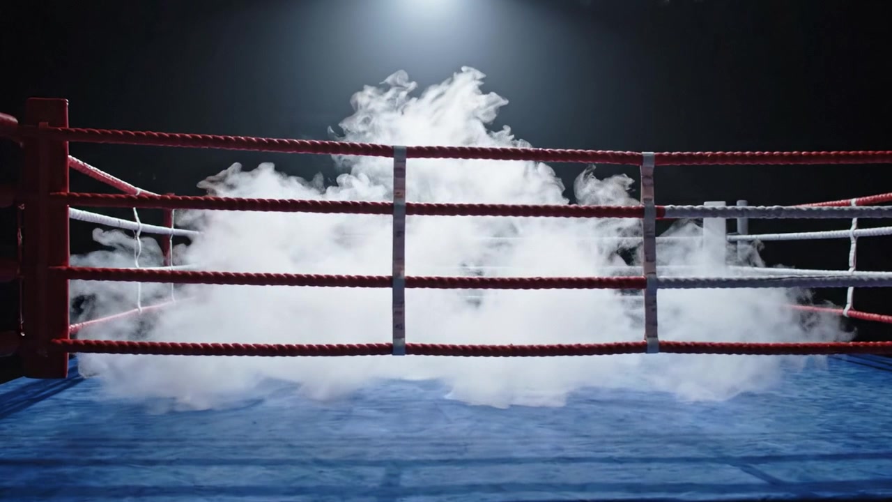 Un dramático ring de boxeo espera la pelea: un lienzo azul reluciente rodeado de cuerdas rojas y blancas bajo una luz misteriosa y humo.