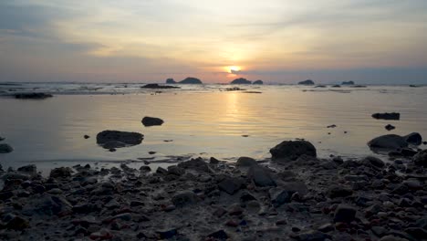 Gentle-ocean-tide-pool-with-calm-water,-rocks-and-islands-in-background-during-sunset