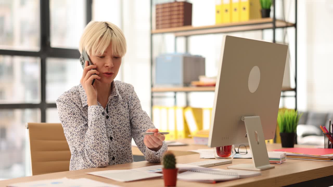 Donna che lavora in un ufficio moderno, parla al telefono e revisiona documenti.
