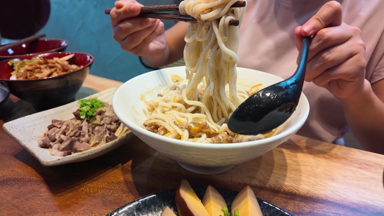 Primo piano di un commensale che solleva noodles da un brodo piccante usando le bacchette a Bangkok.