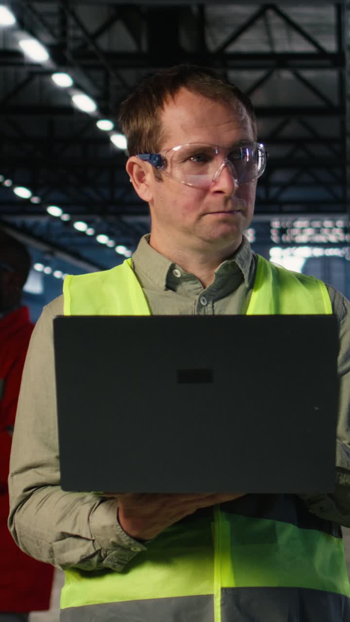 Vertical Video Male engineer supervises workshop fabrication equipment and checking laptop