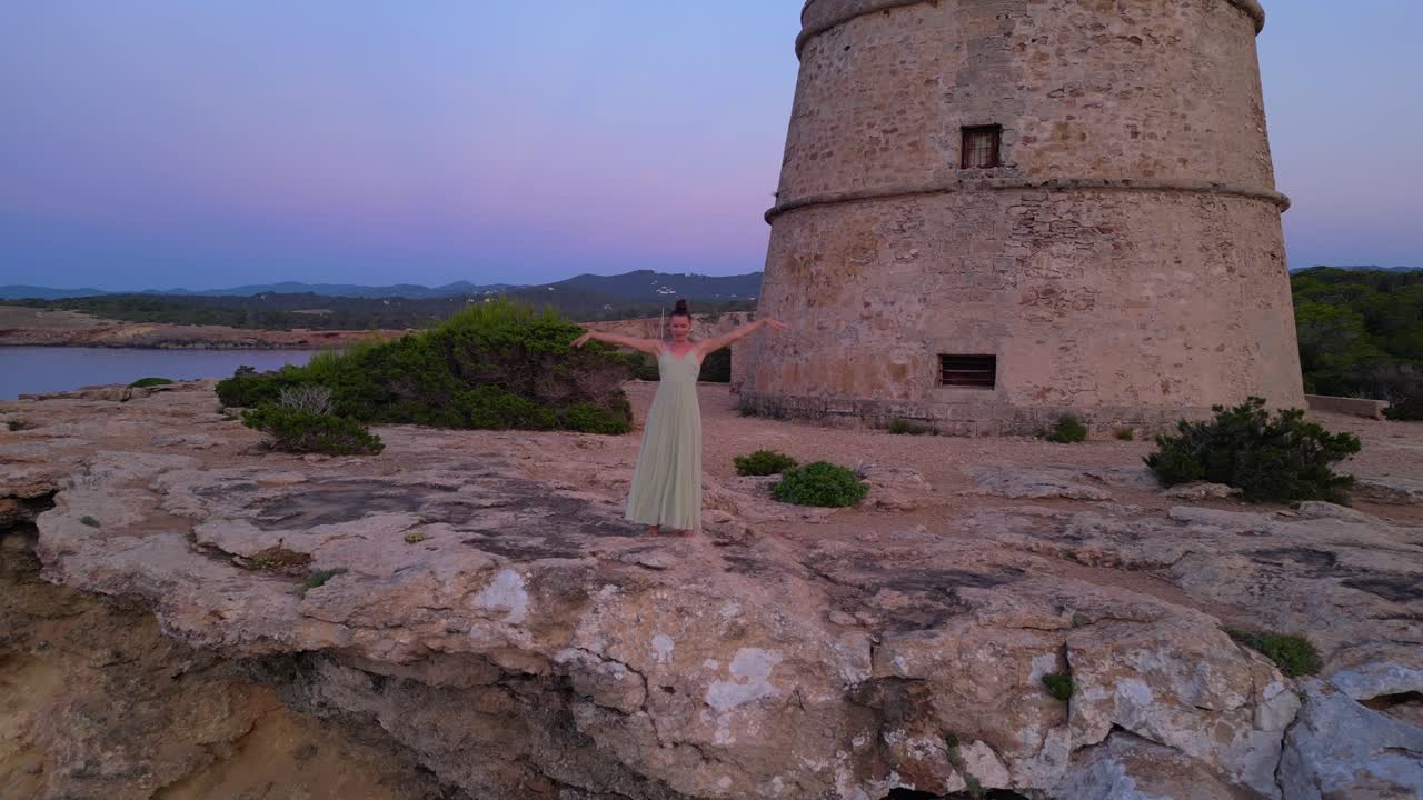 Barefoot hippie girl practicing yoga at sunset near Torre des Carregador, Ibiza, Spain. Fabulous aerial view flight speed ramp hyper motion time lapse
