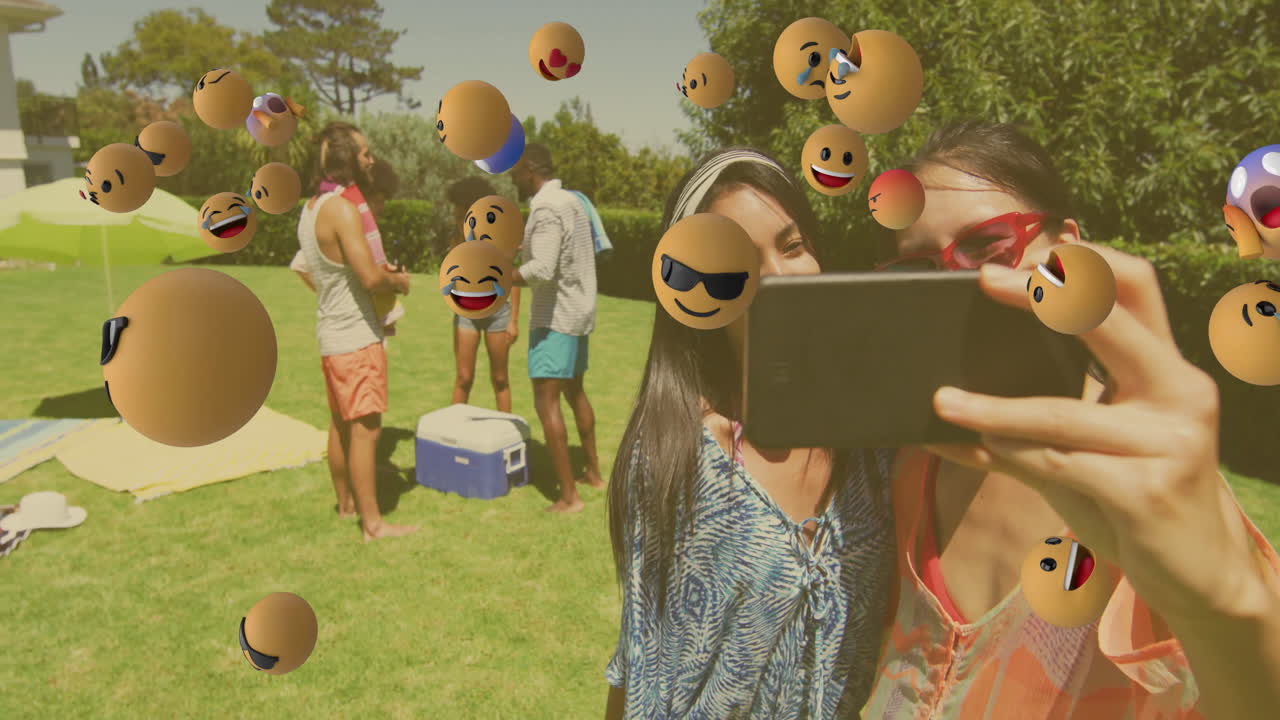 People taking selfie at picnic with floating emoji animation over scene