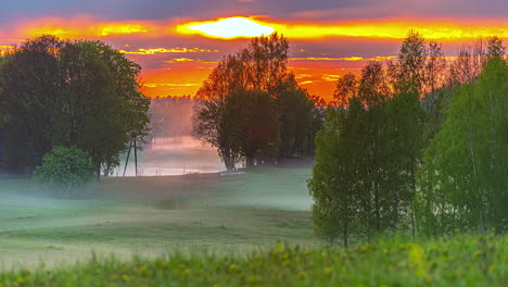 Timelapse-of-scenic-orange-and-golden-sunset-over-the-green-foggy-grasslands-and-trees-in-the-countryside