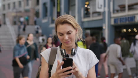 retrato de una mujer turista rubia independiente que usa una aplicación de teléfono inteligente, navega, envía mensajes de texto, disfruta de los viajes por la ciudad, sonriendo optimista