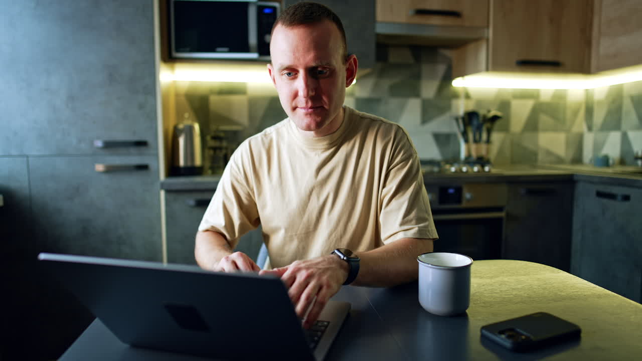 Caucasian male working on laptop in his kitchen. Freelance, remote work from home.