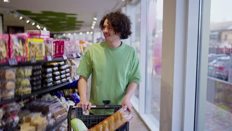 A-brunette-guy-with-curly-hair-walks-with-a-filled-cart-and-chooses-goods-while-shopping-in-a-grocery-supermarket