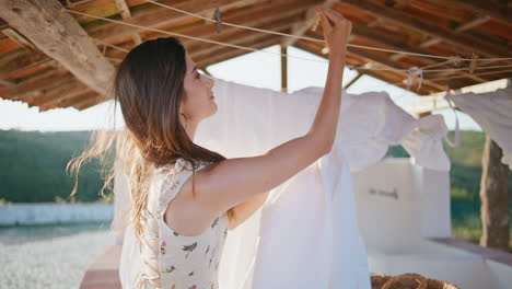 young woman hanging laundry at windy terrace closeup. white linen air drying