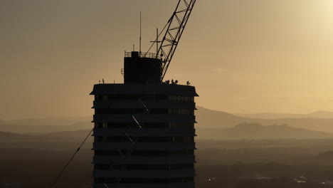 Nahaufnahme-Eines-Hochhauses-Mit-Teleparallaxe-Und-Baukran-Im-Vordergrund-Bei-Sonnenuntergang,-4K-Drohne