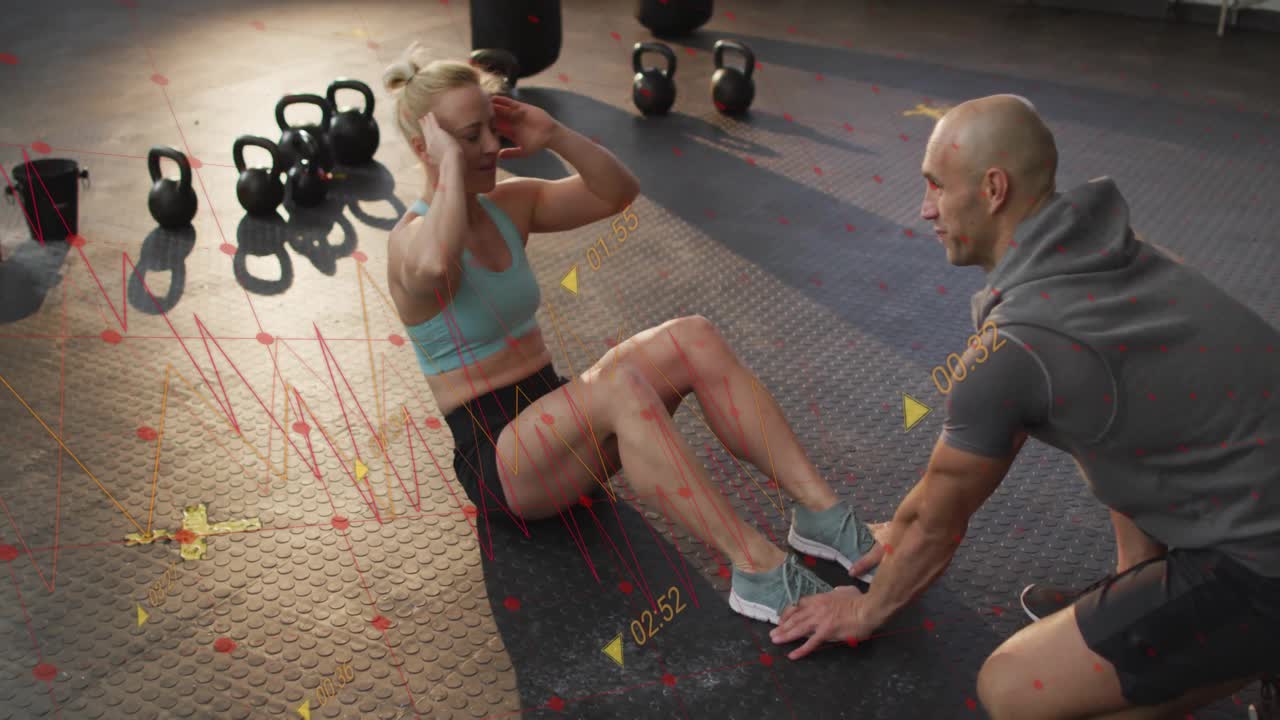 Timer hitting zero starting woman doing crunches near kettlebells with fitness trainer holding feet