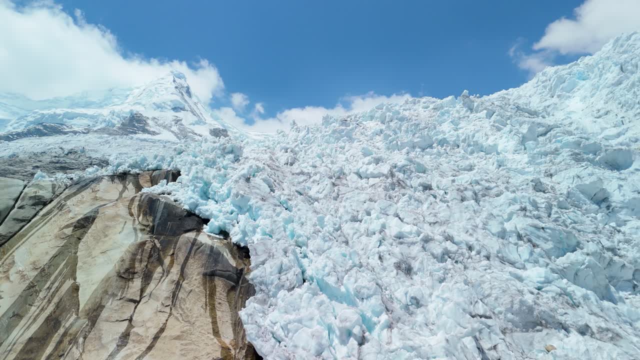 A striking aerial parallax shot reveals the frozen snow-capped peak and fractured glacier ice of Nevado Hualcán in the Cordillera Blanca near Laguna 513