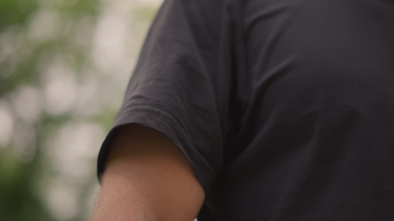 Casual Outdoor Fashion, Man Adjusting Shirt Sleeve Outside, Casual Man Modifying T Shirt Sleeve Amid Park Scenery, Everyday Fashion Snapshot Capturing Man Adjusting His Shirt Outdoors In Nature
