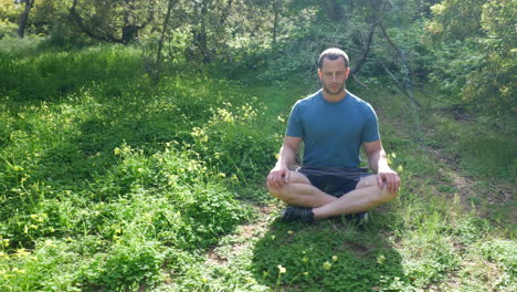 a man sitting in a meditation pose in a green sunny forest meadow practicing deep breathing exercises for stress relier and mental health slow motion