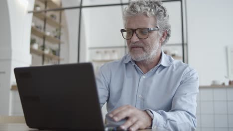 cheerful mature businessman using laptop in co-working interior