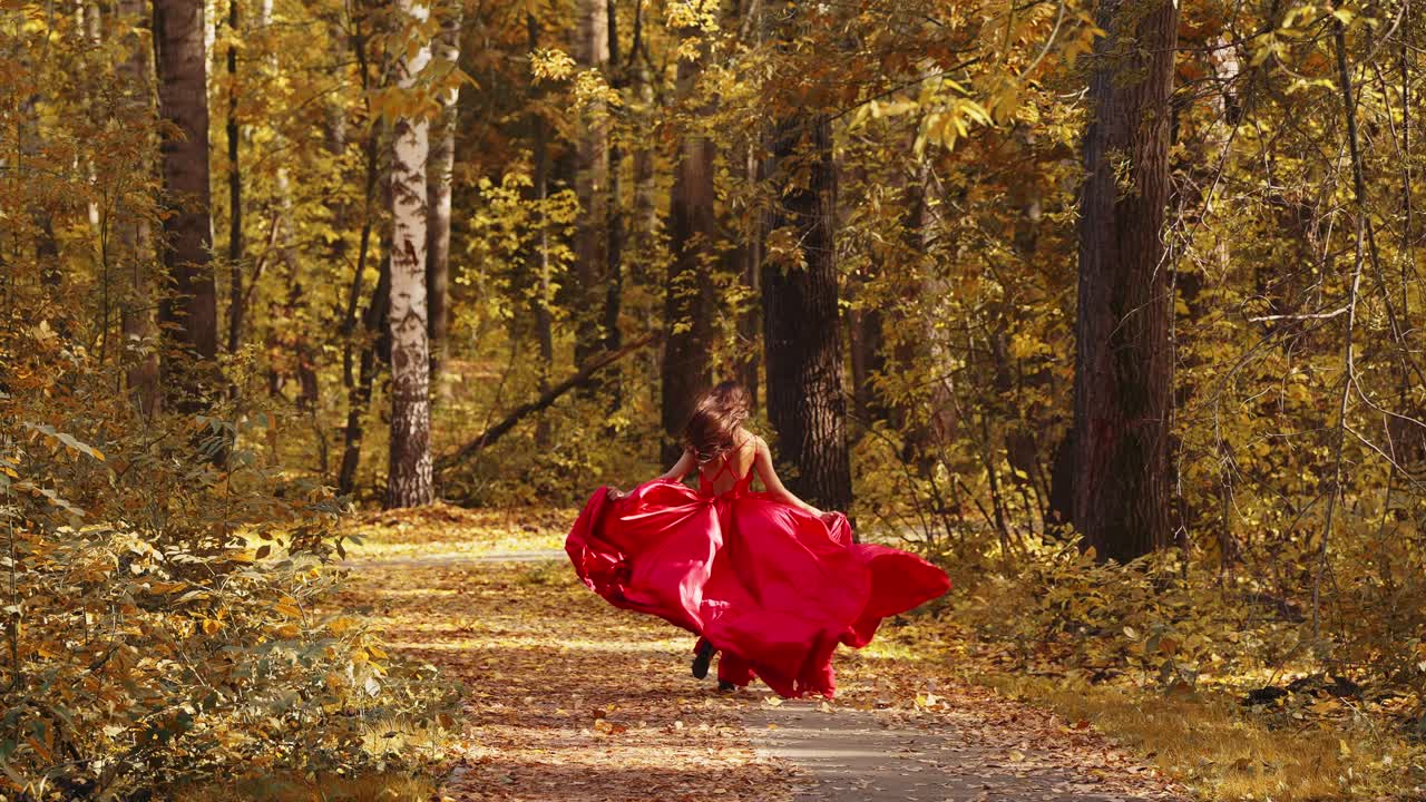 A Graceful Girl in a Vibrant Red Dress Leaps Through a Beautiful Autumn Forest Path, Surrounded by Golden Leaves in a Captivating Dance of Nature and Elegance