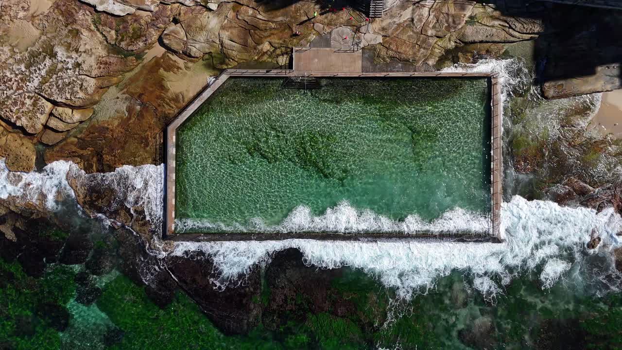 Aerial top down of rock pool surrounded by waves and rocky shoreline in Cronulla, Sydney NSW Australia