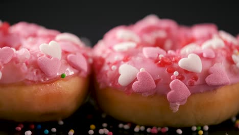 sprinkles falling onto pink donuts with heart shaped sprinkles - sliding shot