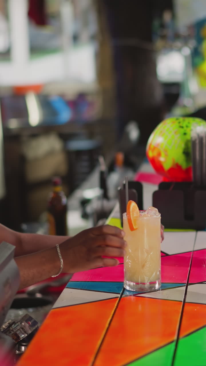 el camarero trata a la mujer con un cóctel en el mostrador de la barra. el camarero negro pone paja en la bebida y da un vaso al invitado en el club. el barman sirve al visitante