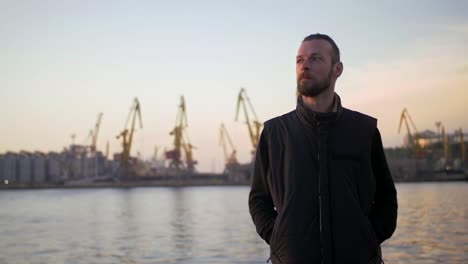 portrait of stylish hipster man on sea port background during sunset, looking aside