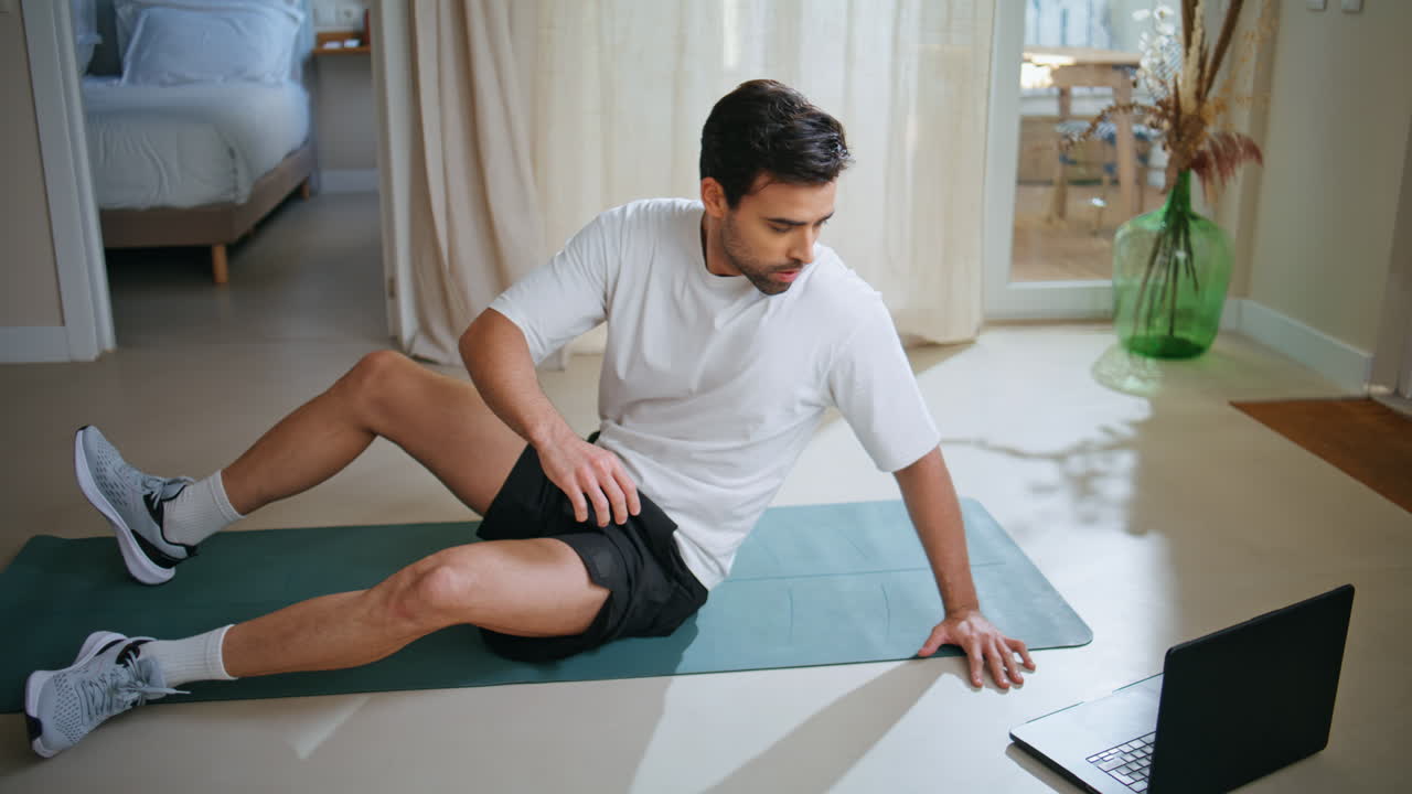 Sportsman watching online video at laptop lying fitness mat. Sporty man workout