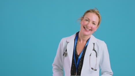 retrato de una doctora sonriente con una bata blanca de pie frente al fondo azul del estudio