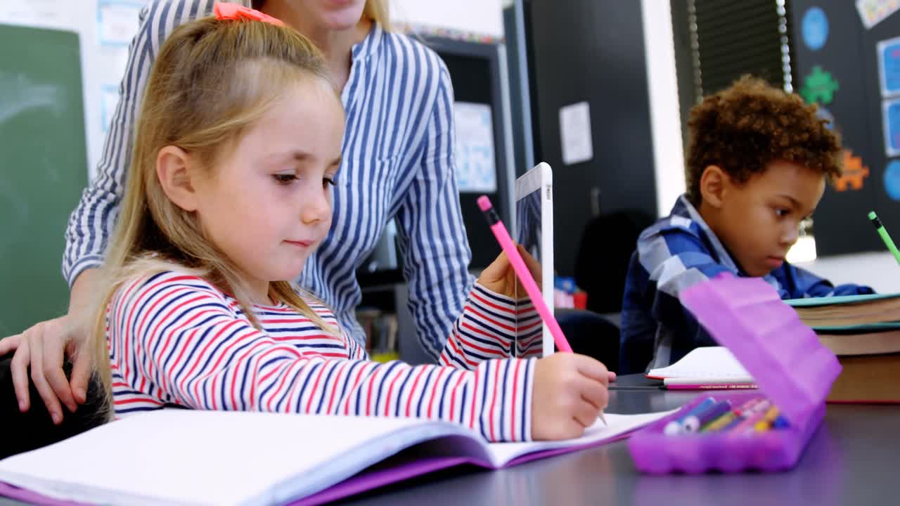 Teacher helping schoolgirl with her homework in classroom