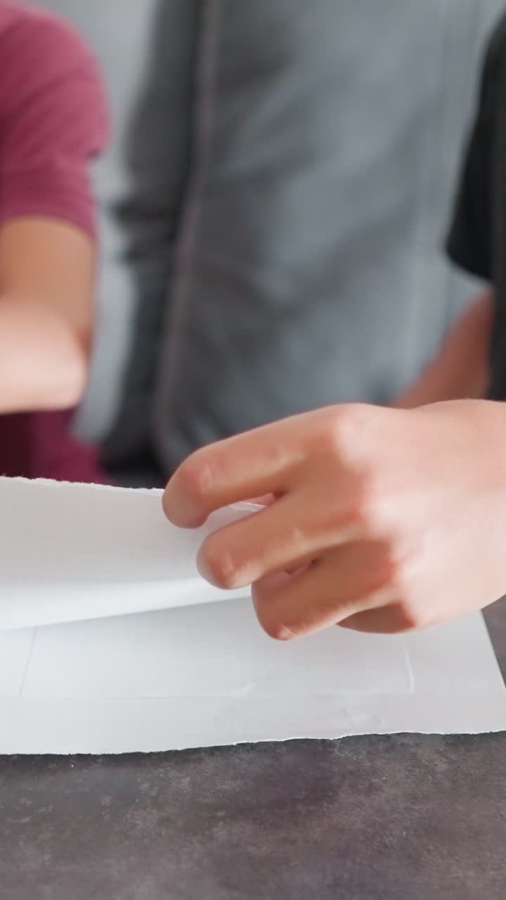 Primer plano de una niña escribiendo en un portátil mientras un niño a su lado escribe en un papel con un bolígrafo y luego muestra con orgullo su trabajo; ella echa un vistazo y le da el visto bueno con un gesto de apoyo.