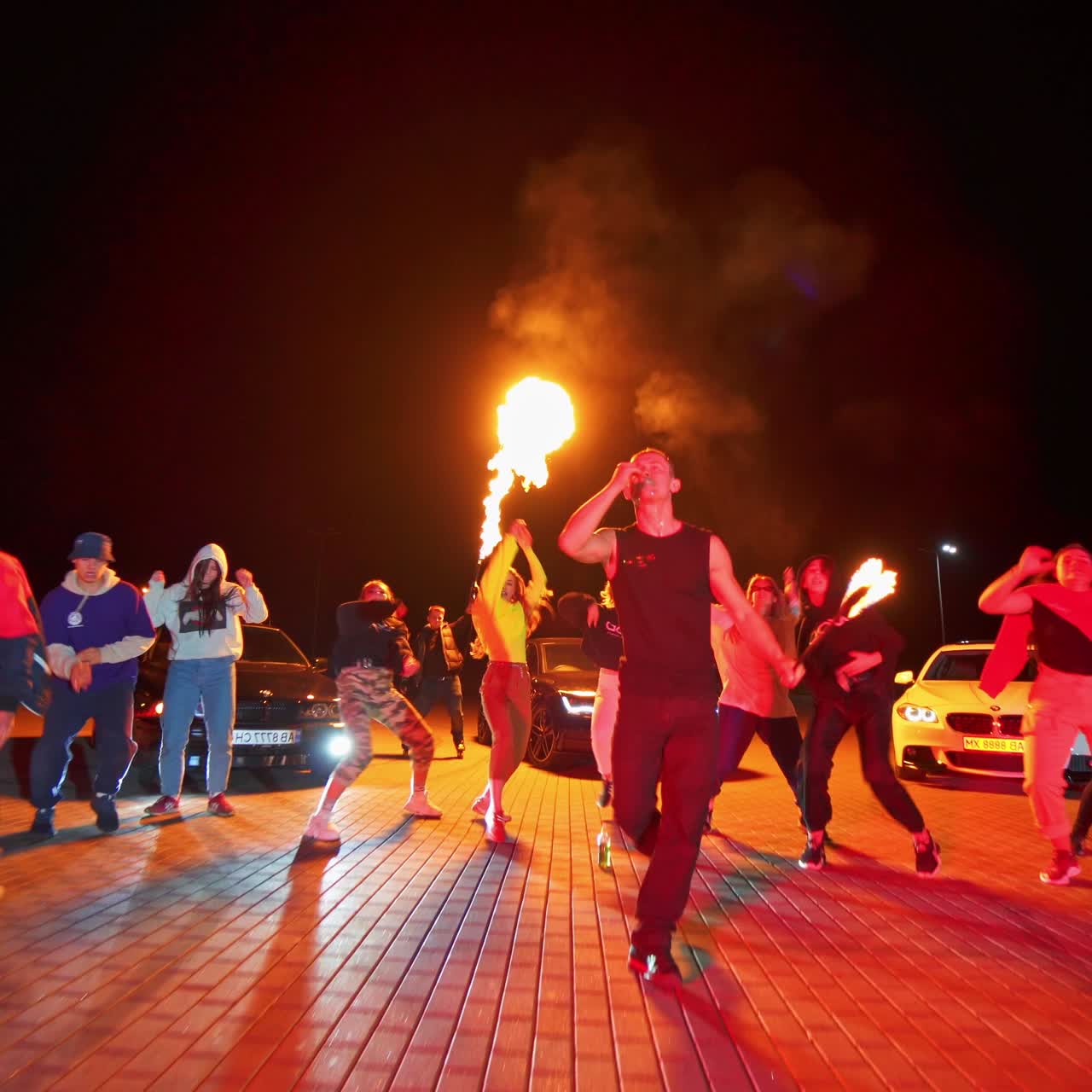 Hip hop party outdoors at night. Group of teenagers performing in stylish clothes. Man in the middle presents fire show