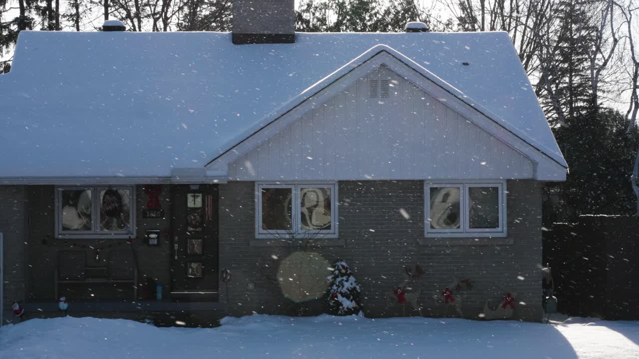 Snow flakes fall in front of sunny suburban house, slow motion handheld.