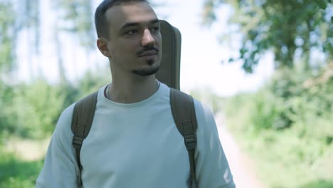 young man walking with guitar on street near forest