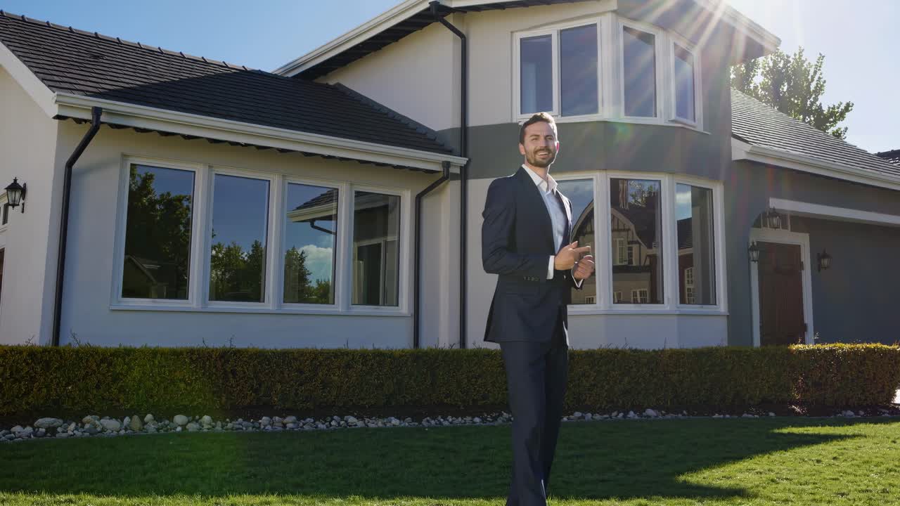 A man in a suit gestures in front of a modern house, captured from a low angle with sunlight